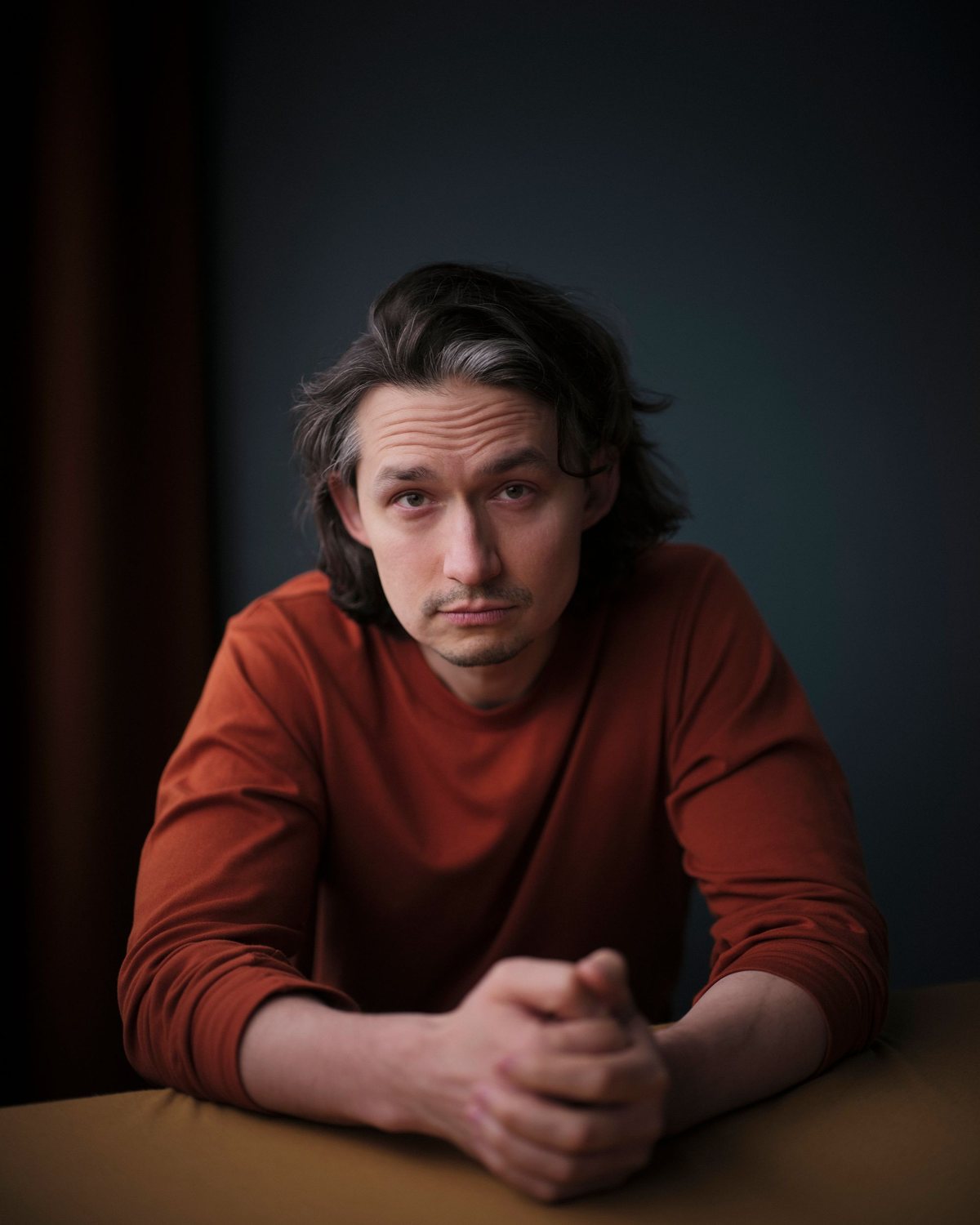 Michael Golab, seated at a table in a rust jumper, hands clasped, looking into the camera